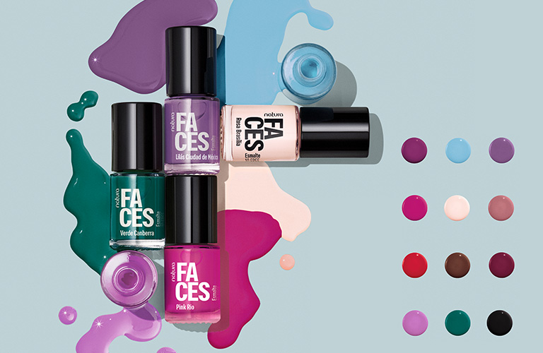 Foto de esmaltes Natura Faces sobre fondo celeste. Cuatro frascos en colores verde, púrpura, rosa y nude con manchas de esmalte derramado. A la derecha, una paleta de doce puntos de colores muestra la variedad de tonos disponibles.